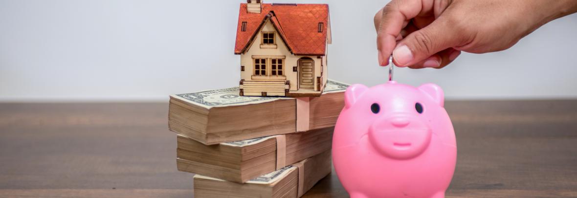 Toy home on top of money beside a piggy bank