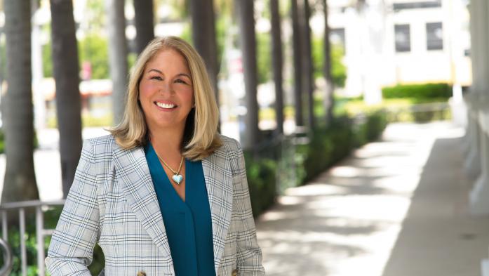 Shot of Christine Hansen. Standing outside. Wearing a plaid blazer with right hand in pocket