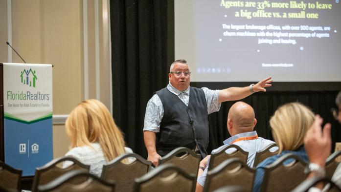 Man with arm extended speaking to a room of people