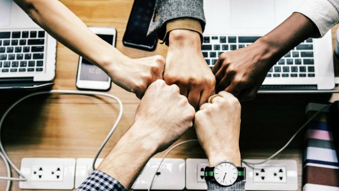 Team of people fist bumps over computers and coffee.