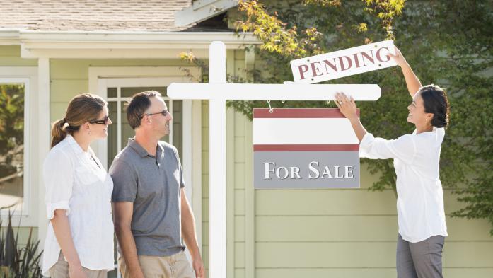 Couple watches their Realtor add a pending sign to a home's for-sale sign
