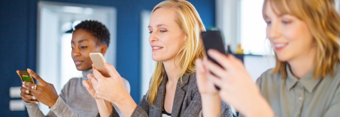 three women in office using cell phones