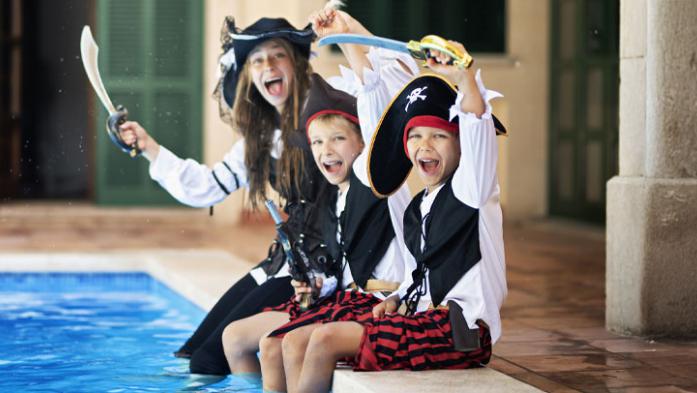 Three kids dresses as pirates dip their feet in a swimming pool